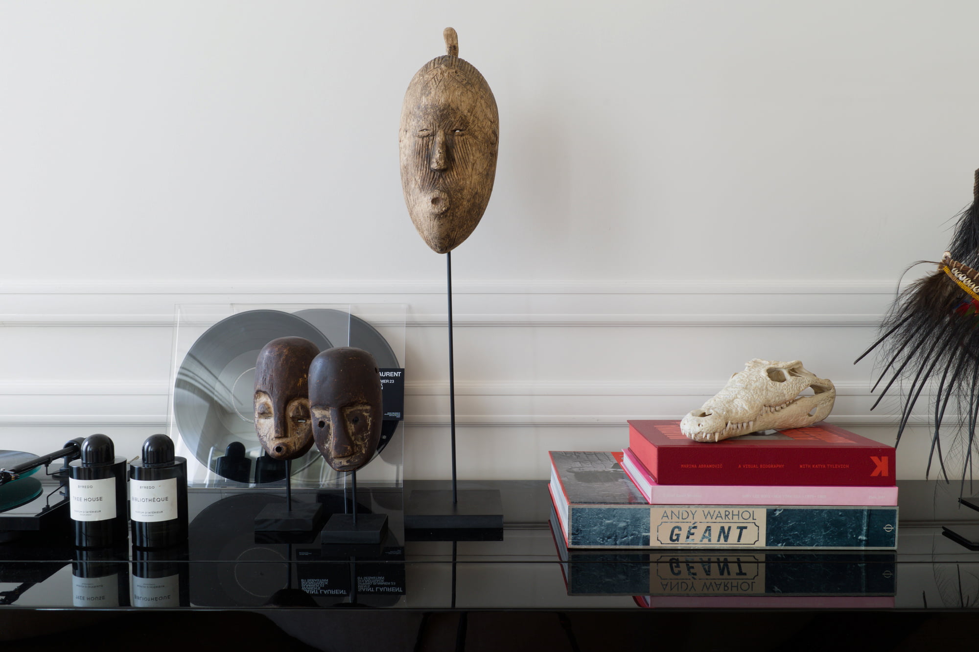 African masks, books, candles, and decorative objects arranged on a glossy black cabinet.