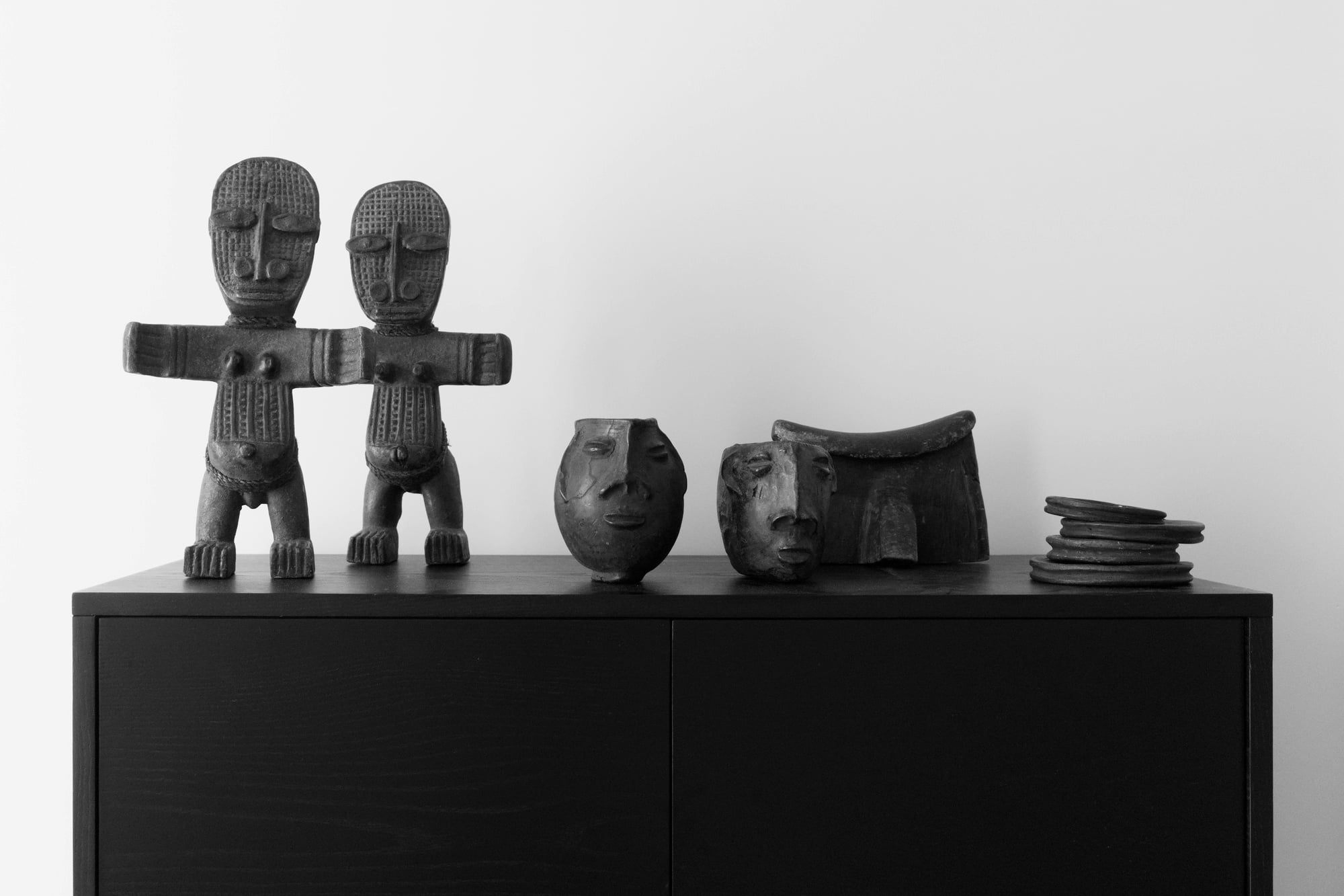 Collection of African sculptures and carved objects displayed on a black cabinet.