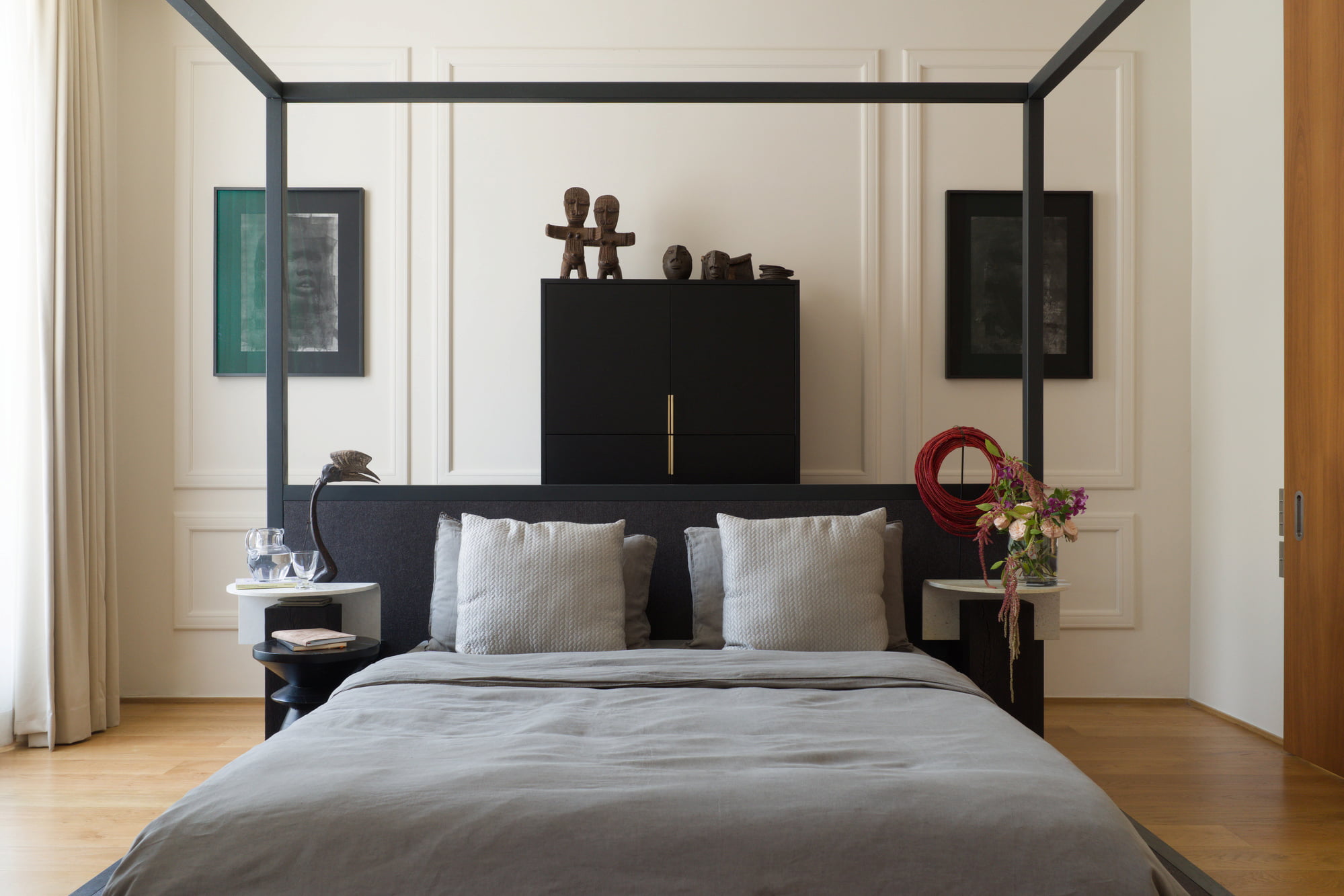 Canopy bed framed by African sculptures and contemporary furnishings.