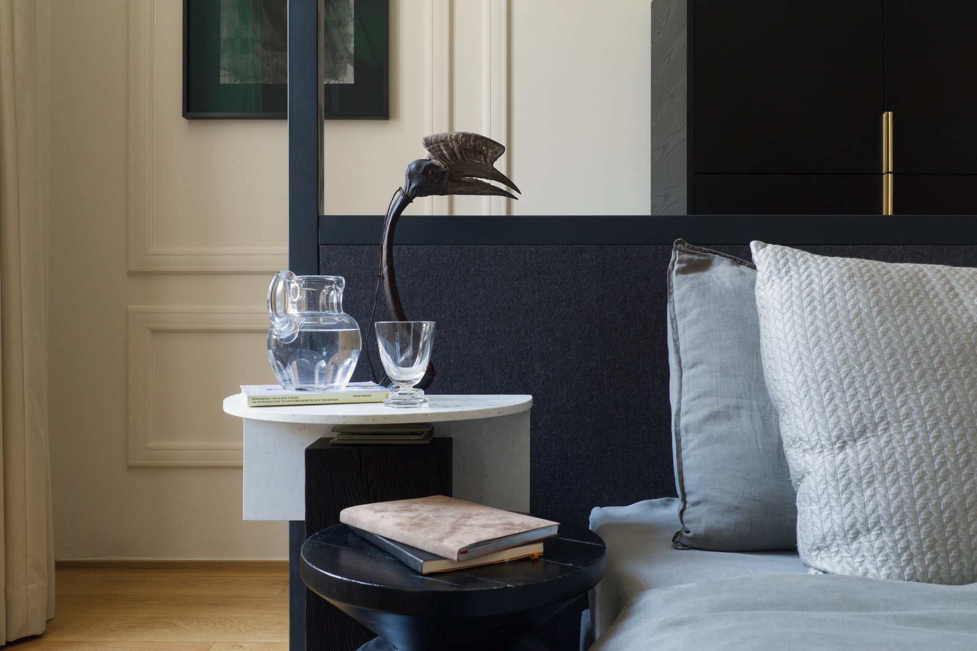 Bedside table with glassware, books, and a carved bird sculpture.