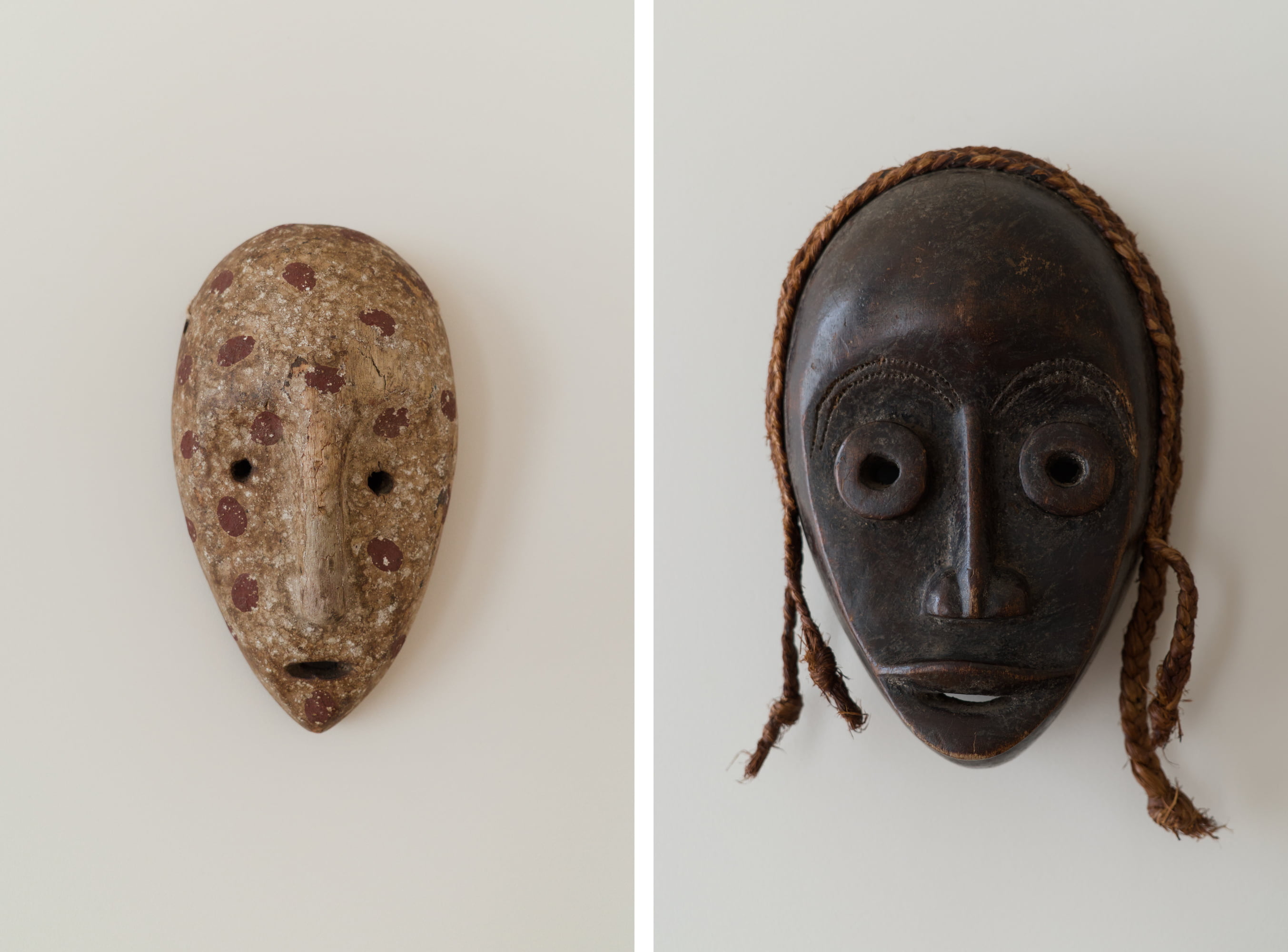 Two African masks mounted side by side on a white wall.