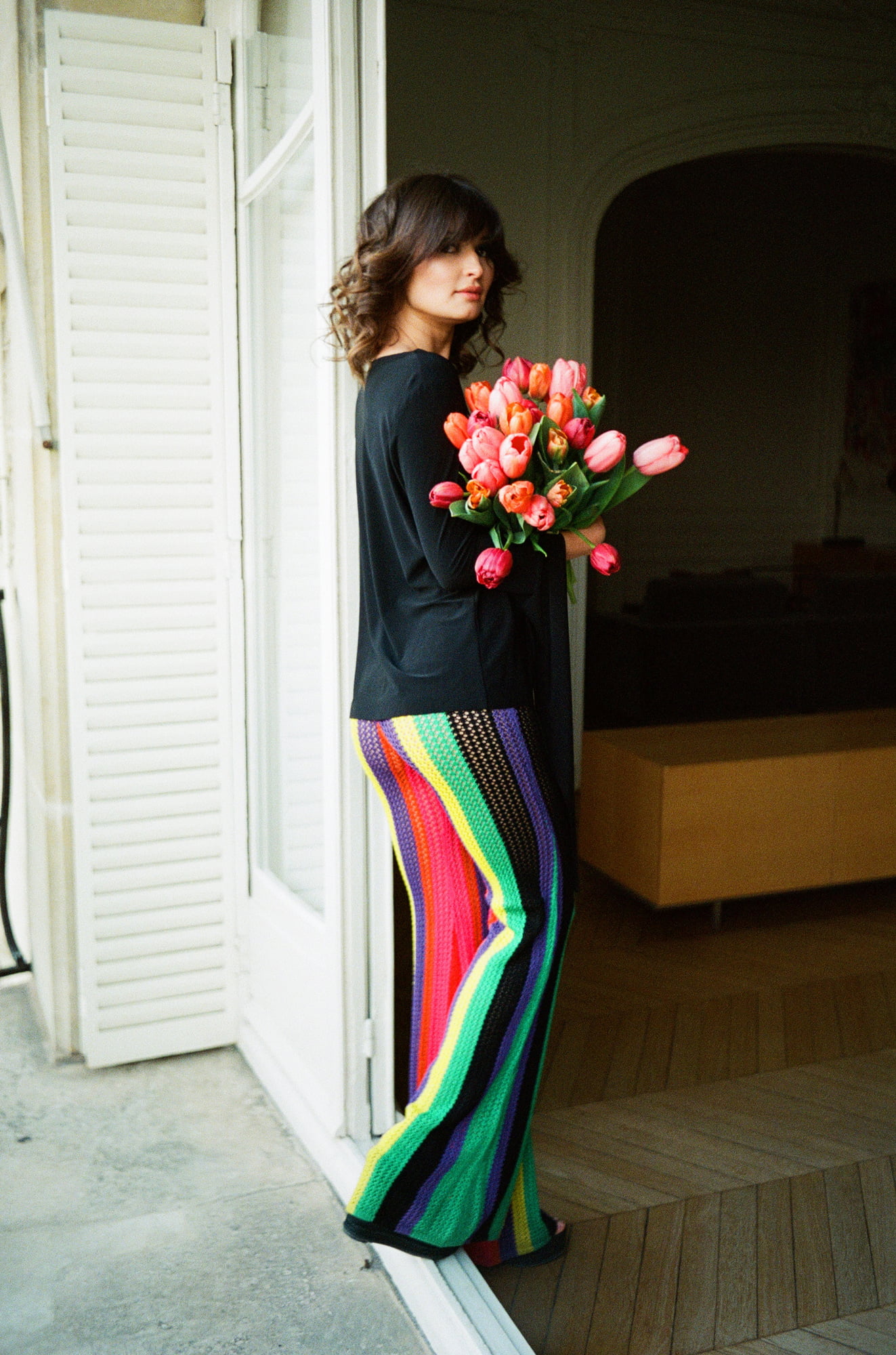 Ariadna standing by an open balcony door holding tulips at an apartment in Invalides, Paris