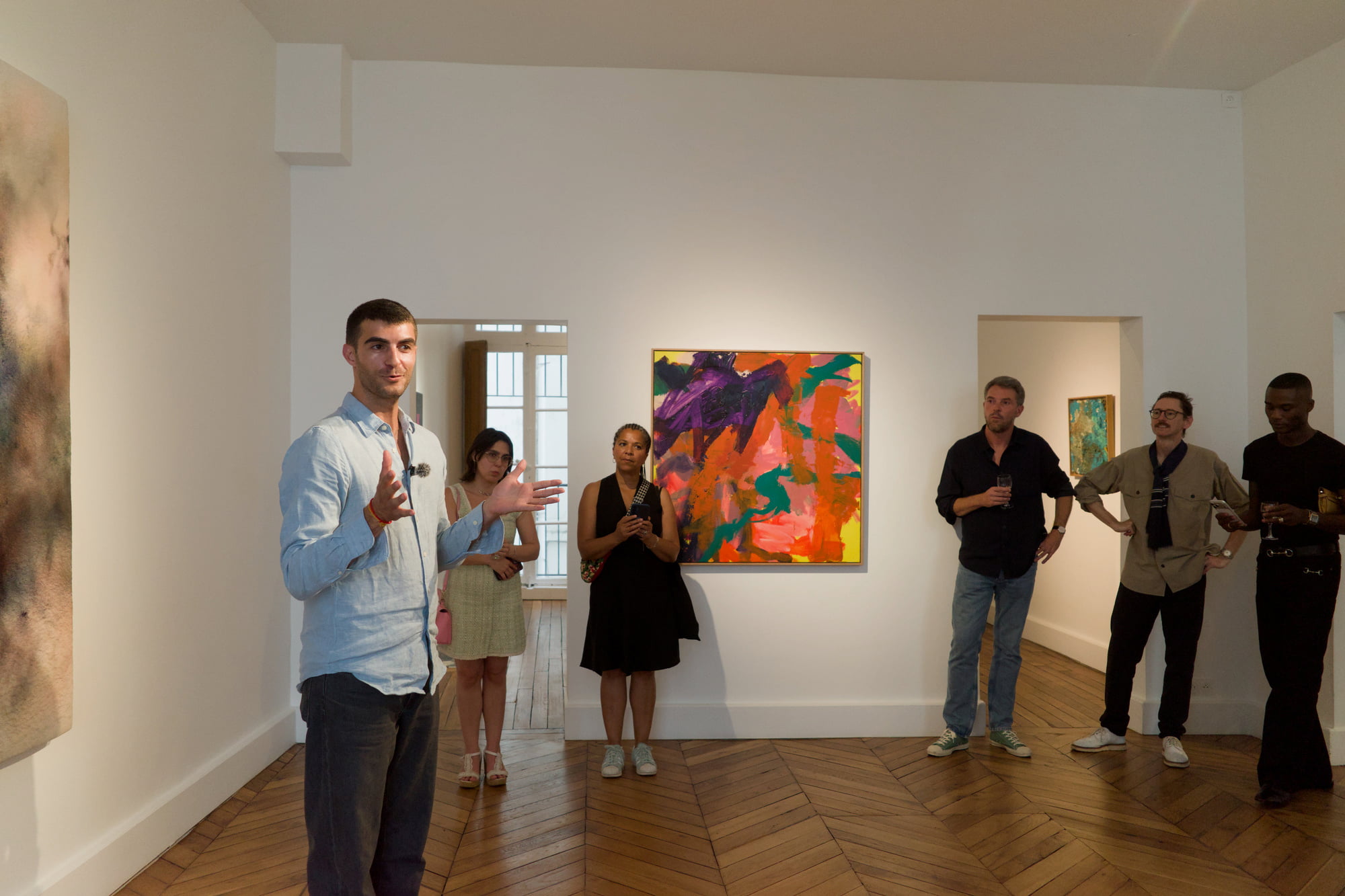 Hugo Giacometti addressing guests gathered around a colorful abstract painting during Arty House