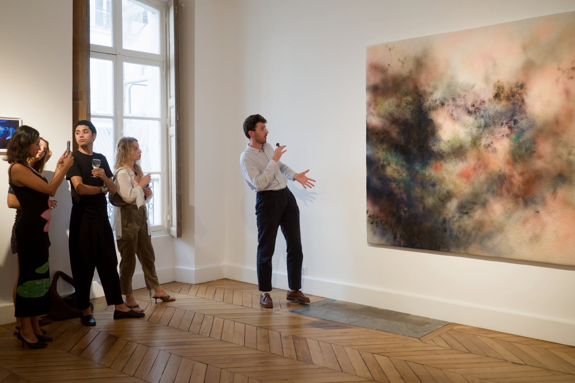 Armand Camphuis presenting a large abstract artwork to guests in a Paris gallery