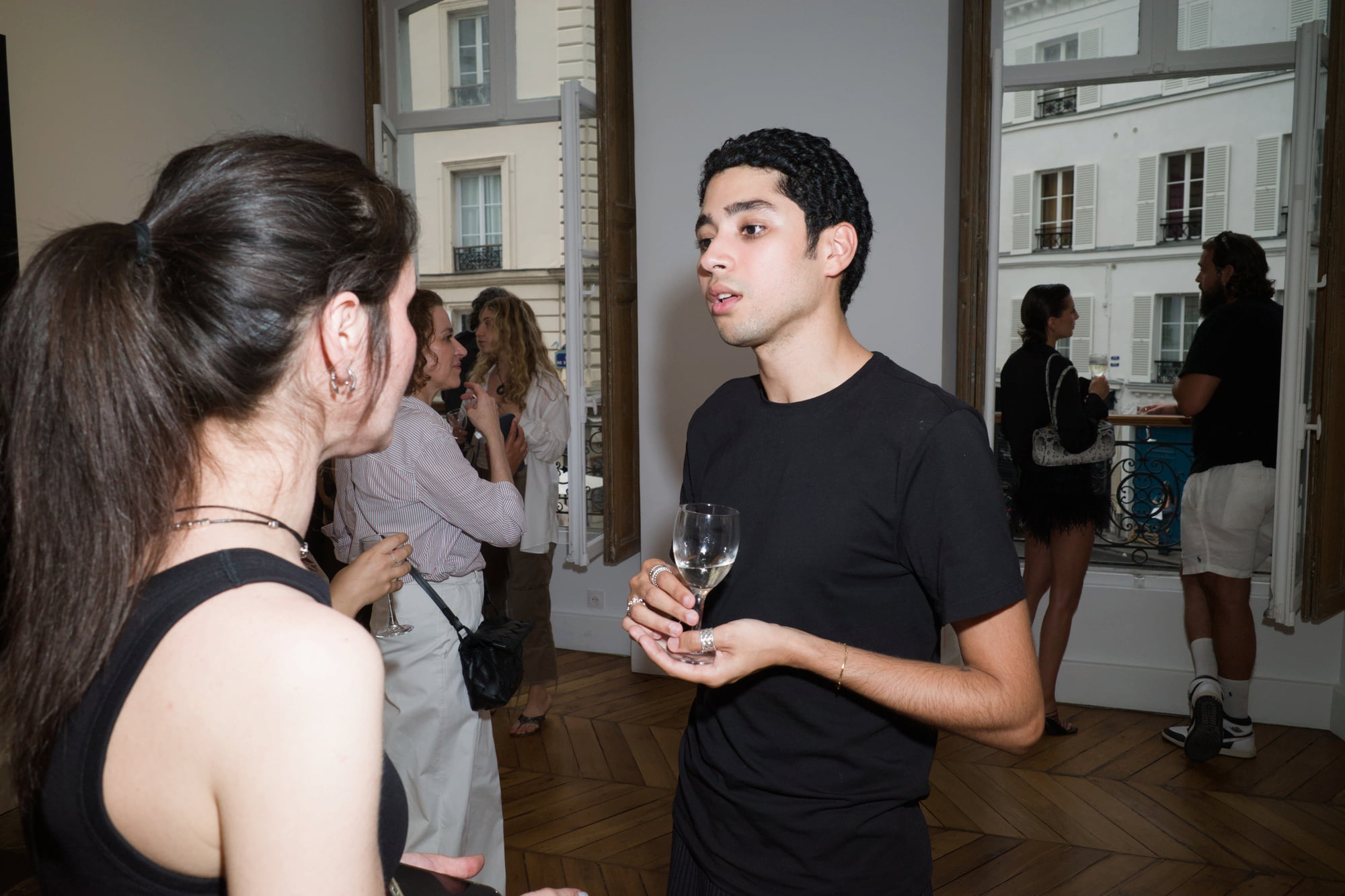 Saad Ahellal holding a glass of wine while talking with a guest beside open gallery windows