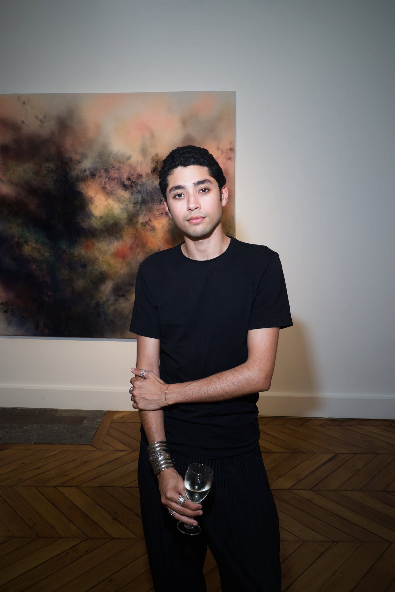 Portrait of Saad Ahellal dressed in black standing in front of an abstract painting