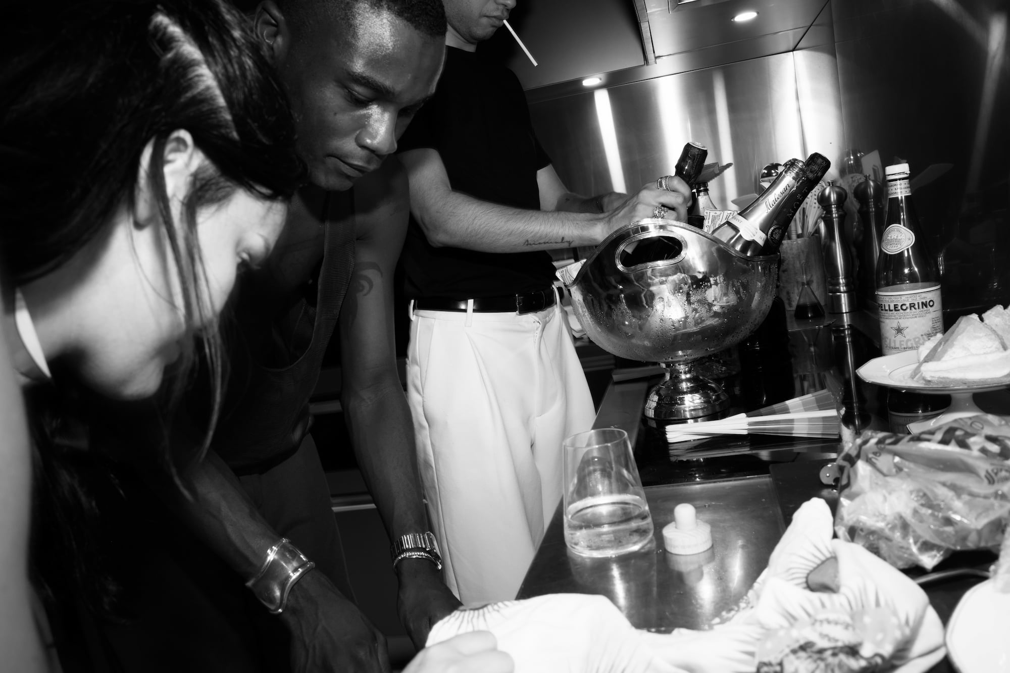 Guests preparing drinks together around a kitchen counter filled with bottles and glasses.