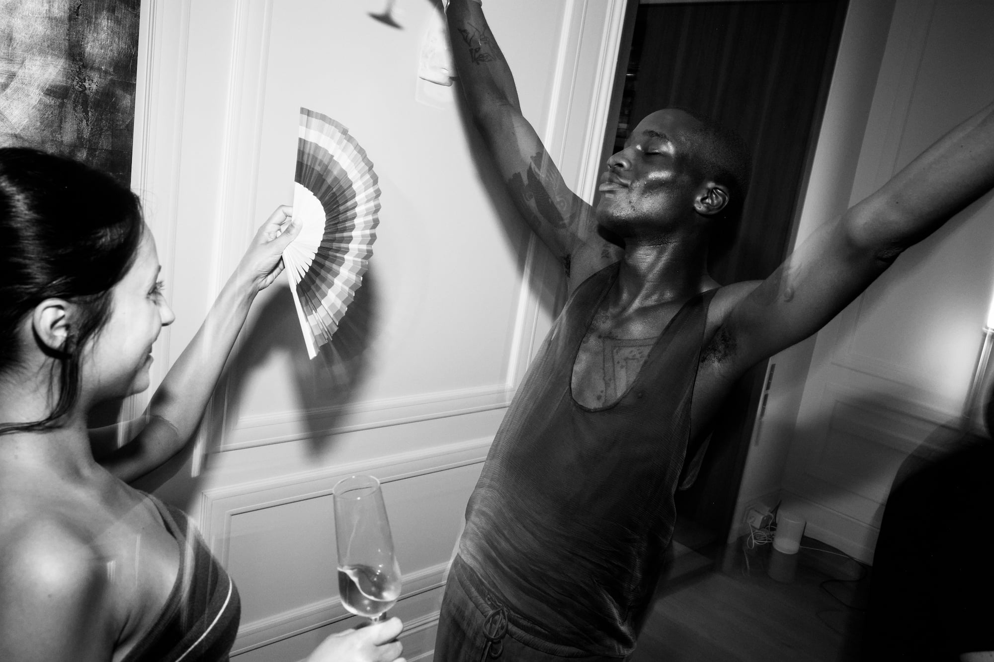 Guest dancing with raised arms while another cools him with a folding fan.
