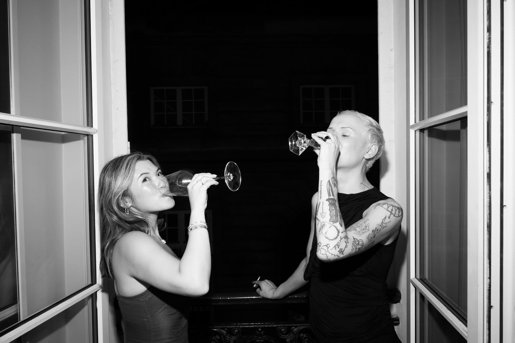 Two guests drinking wine together by an open window overlooking the night.