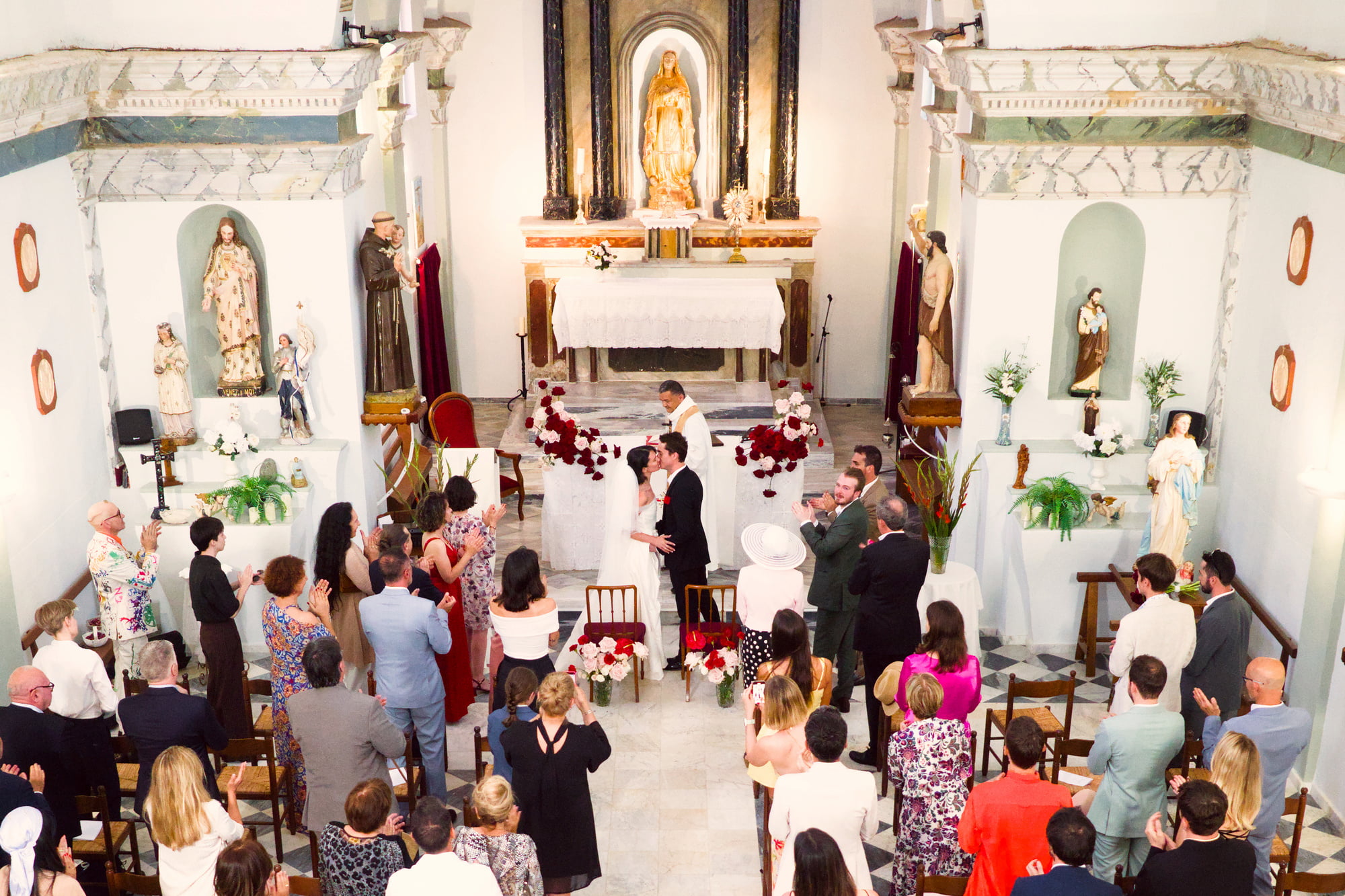 Gabriel and Eléa kissing at the altar as guests applaud inside the village church.