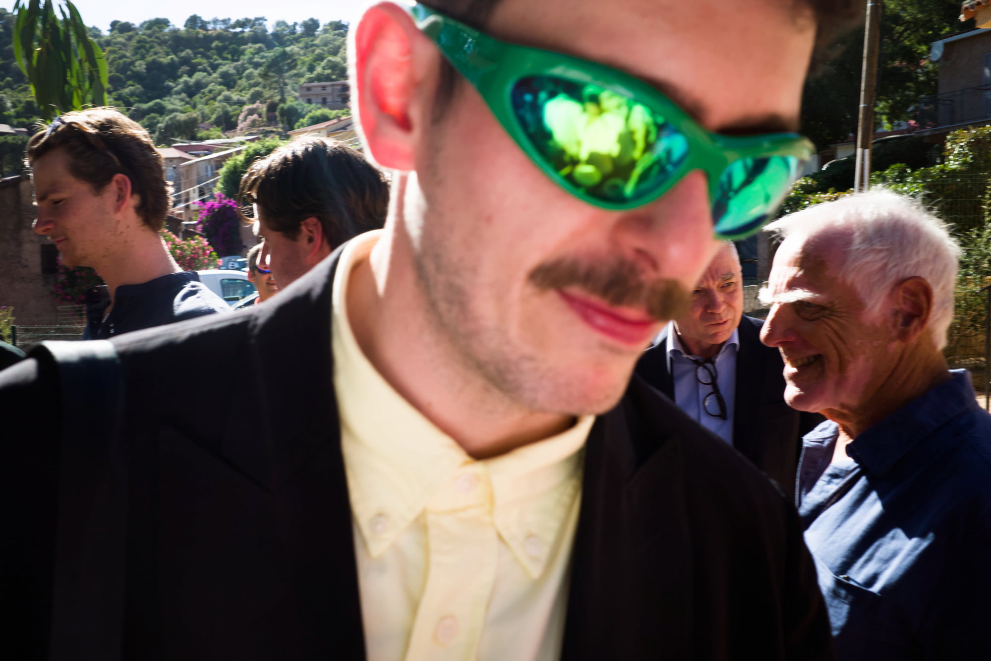 Close portrait of a wedding guest wearing bright green sunglasses among the crowd.