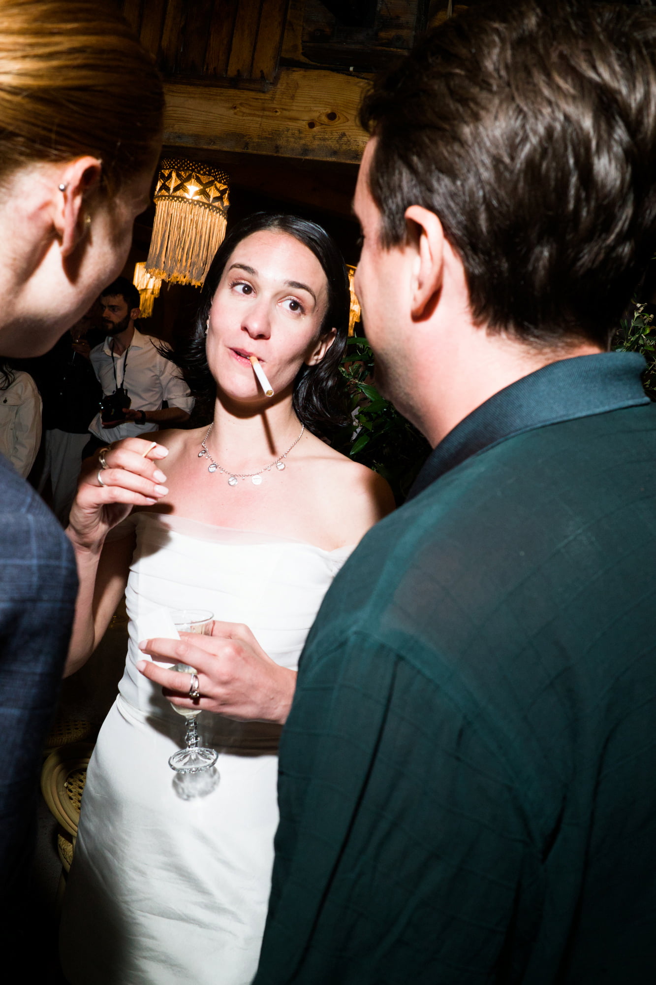 Eléa holding a drink and smoking while speaking with guests during the evening reception.