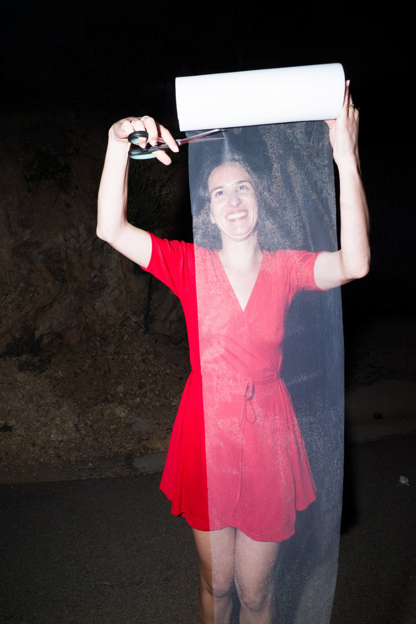Woman in a red dress cutting a long strip of white tulle at night.