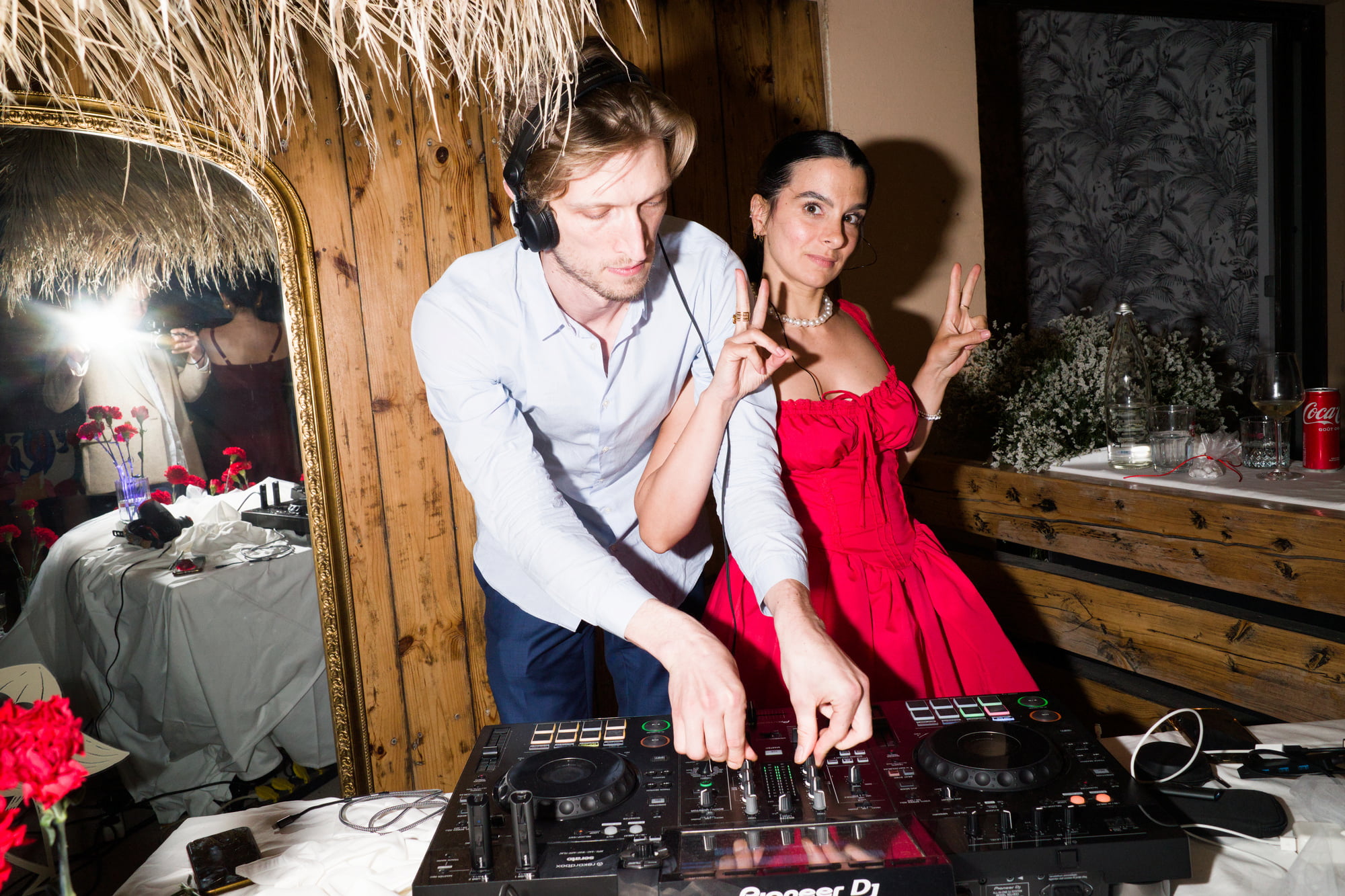 DJ mixing music as a woman in a red dress poses beside the booth.