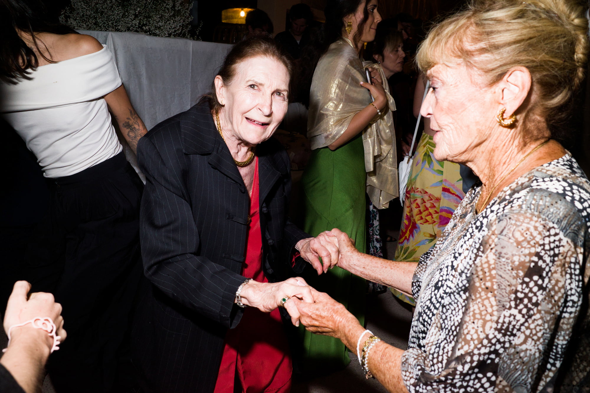 Two older women holding hands and dancing together during the wedding party.
