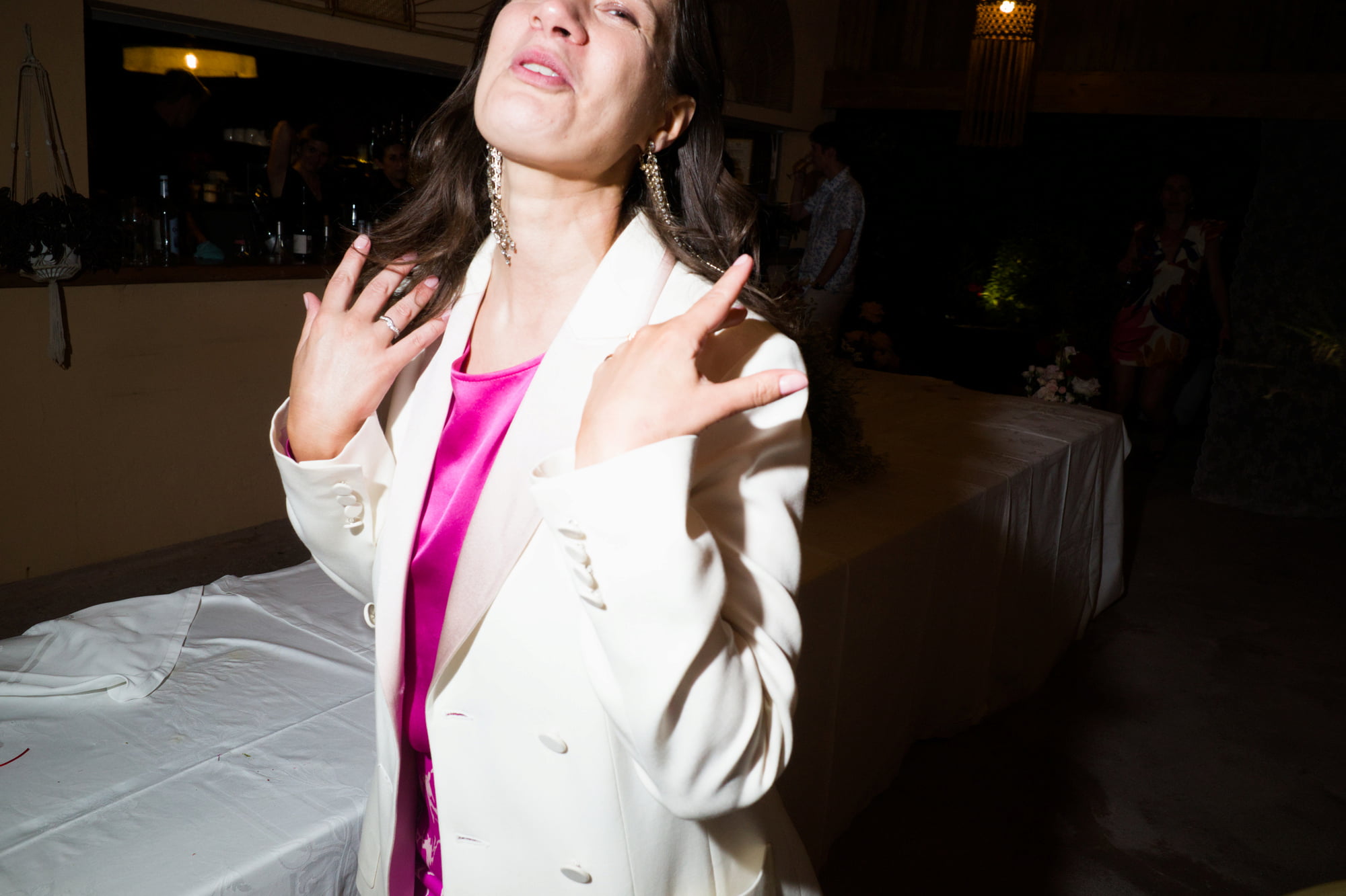 Wedding guest in a white blazer and pink dress dancing toward the camera.