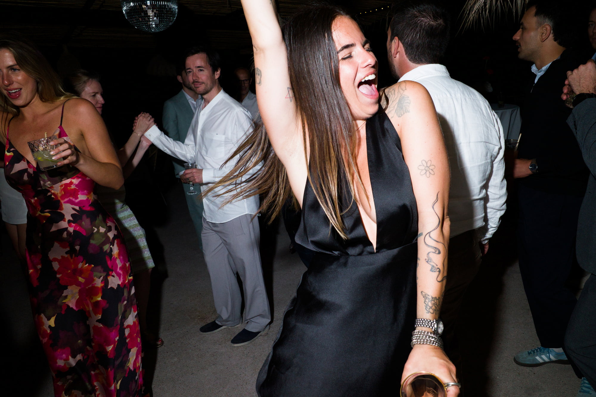 Woman in a black dress dancing with one arm raised among wedding guests.