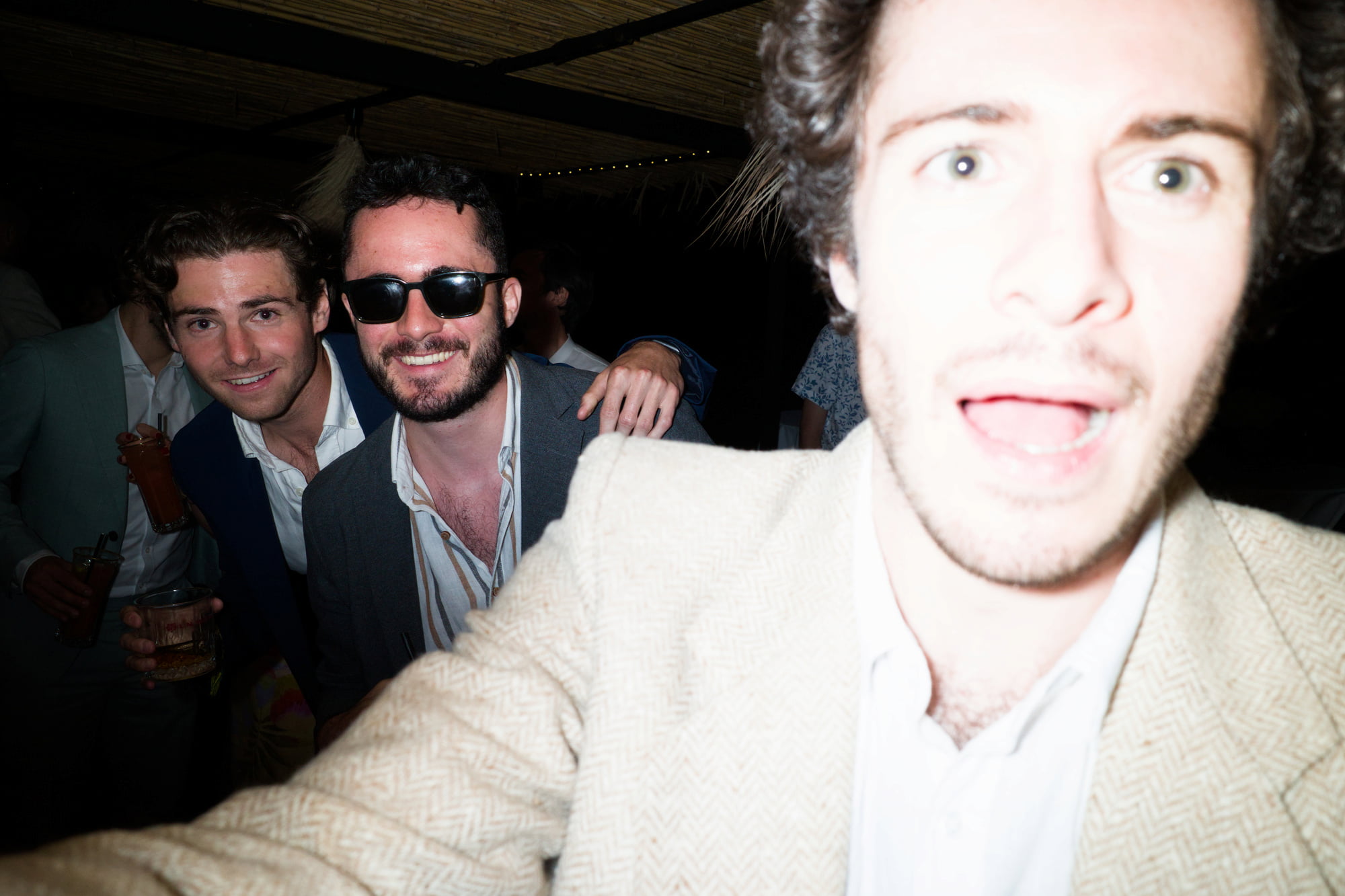 Three wedding guests posing for the camera, with one face brightly overexposed by the flash.