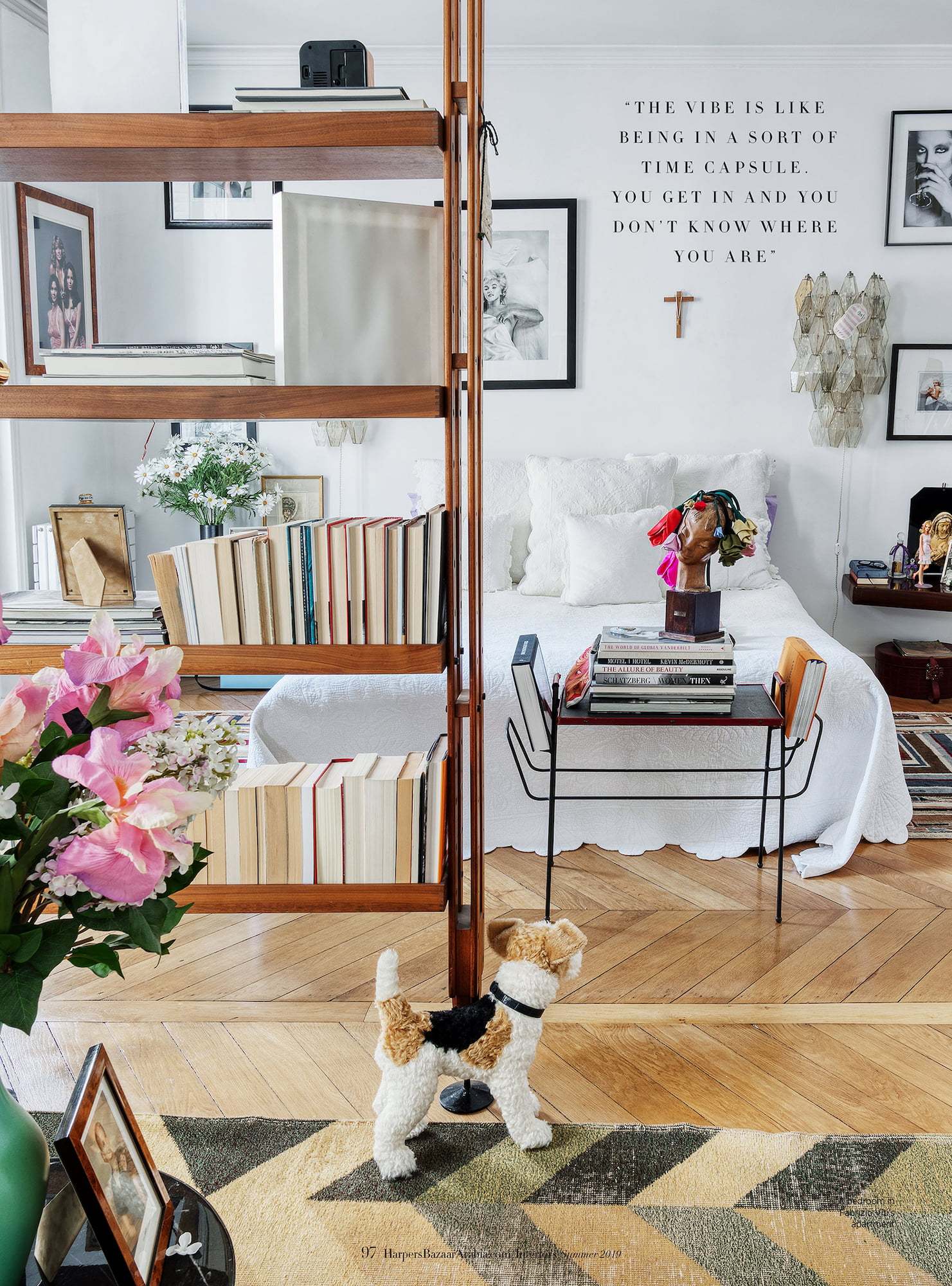 Bedroom in Fabrizio Viti’s Paris apartment with bookshelves, framed photographs, flowers, white bedding, and a small dog sculpture