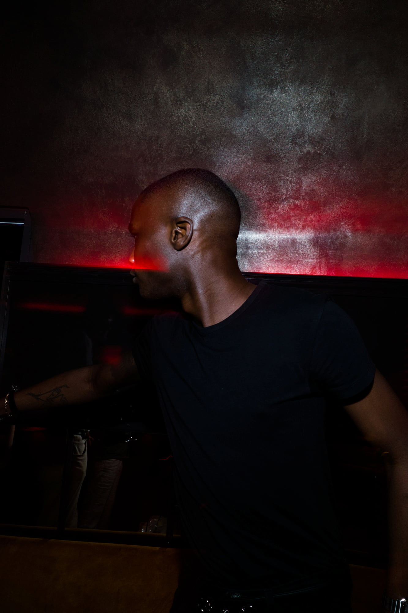 Man in a black T-shirt turning his head as a red beam of light crosses his face in a dark nightclub.