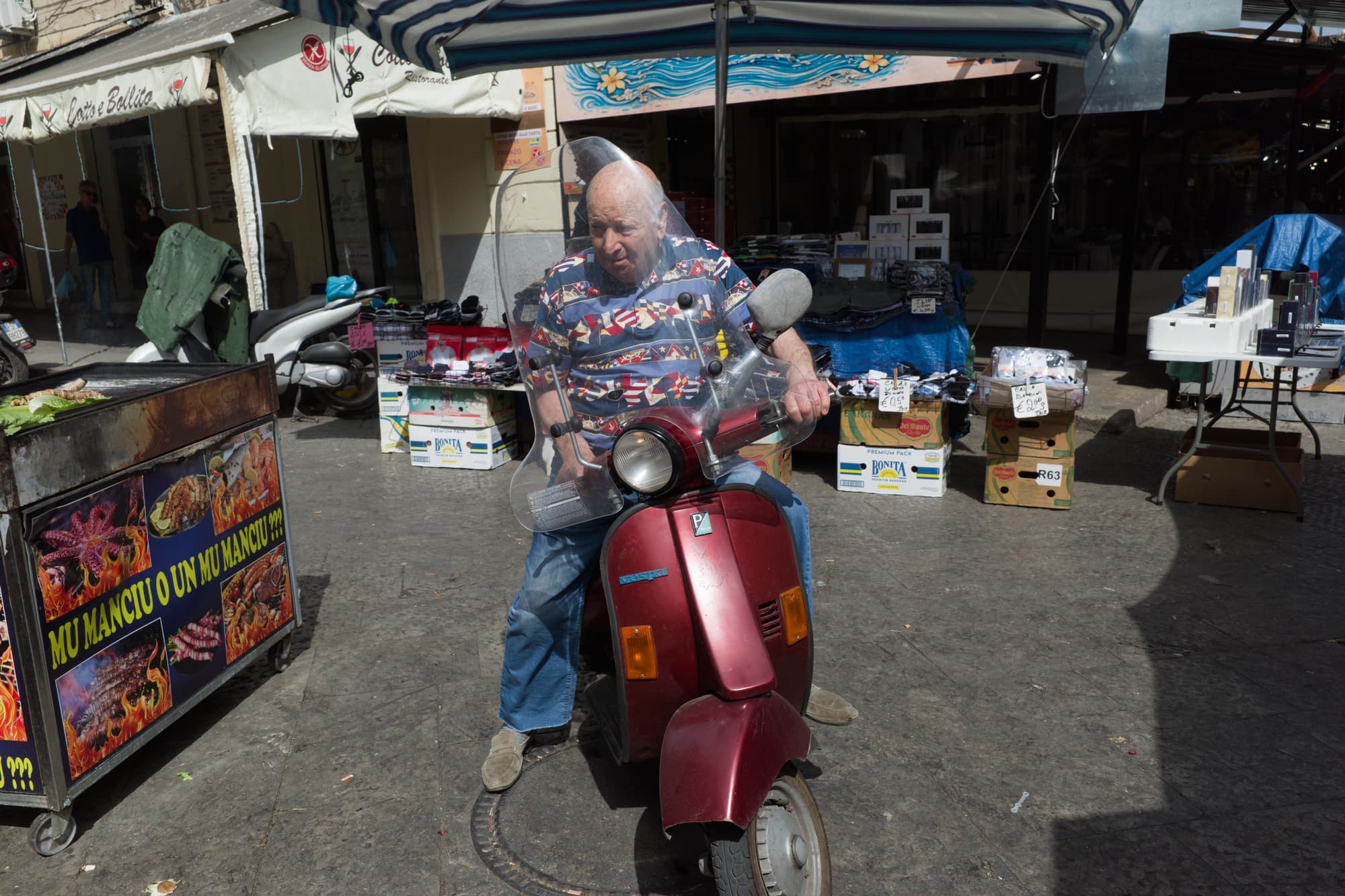 Man seated on a red scooter in a Palermo market street