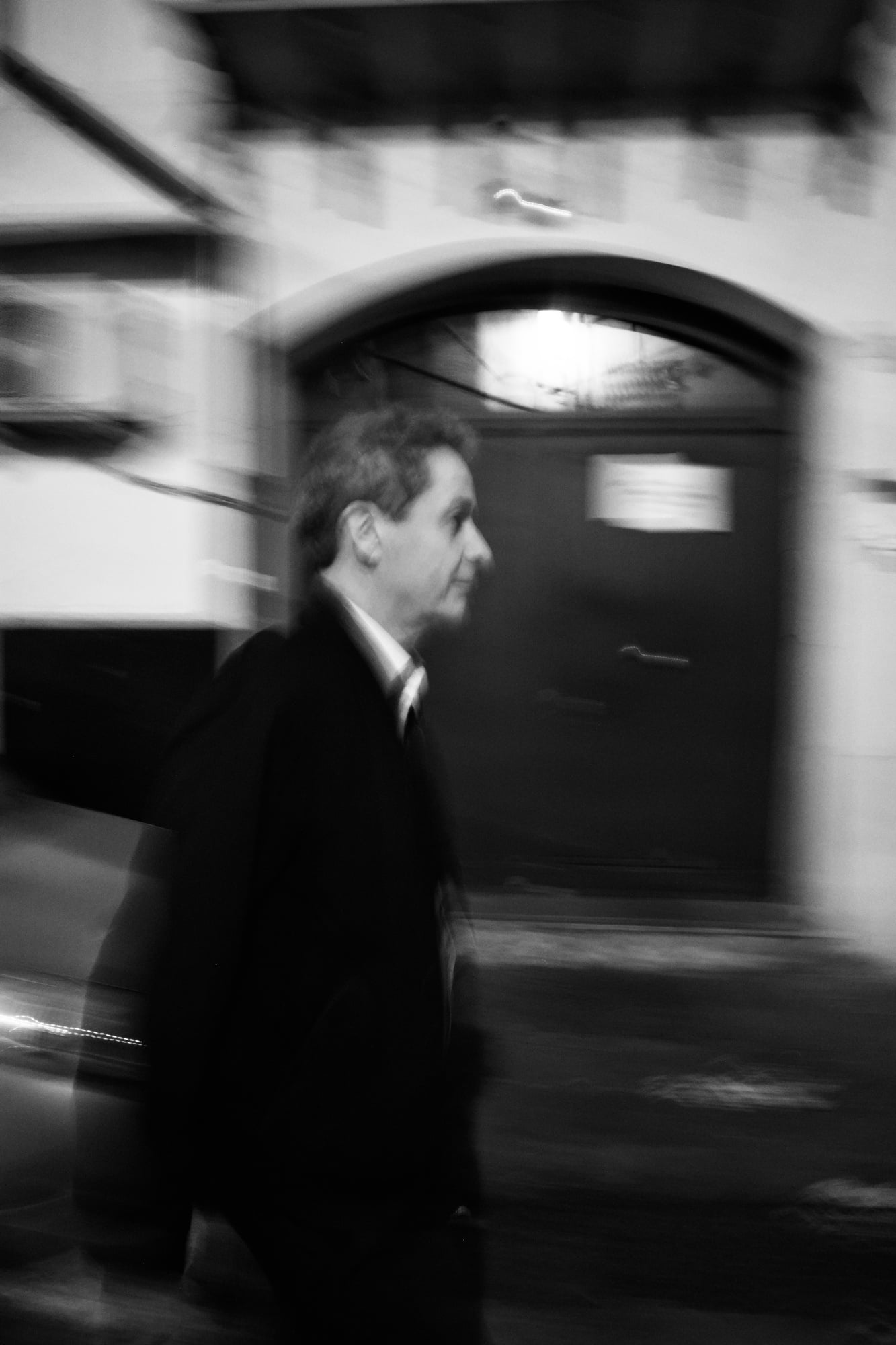 Black-and-white blurred street portrait of a man walking past an arched doorway in Palermo