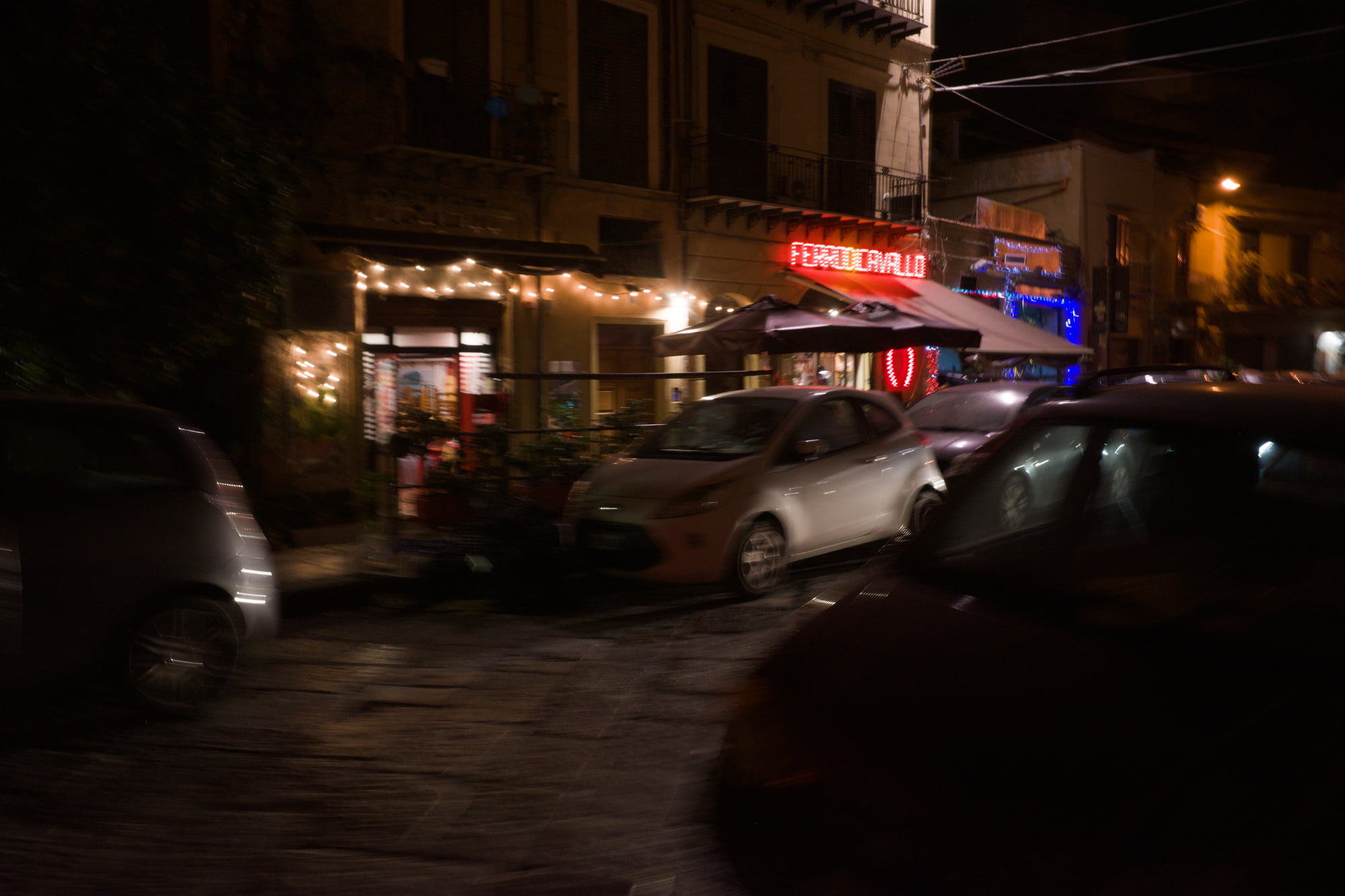 Night street scene in Palermo with parked cars, restaurant lights, and wet pavement