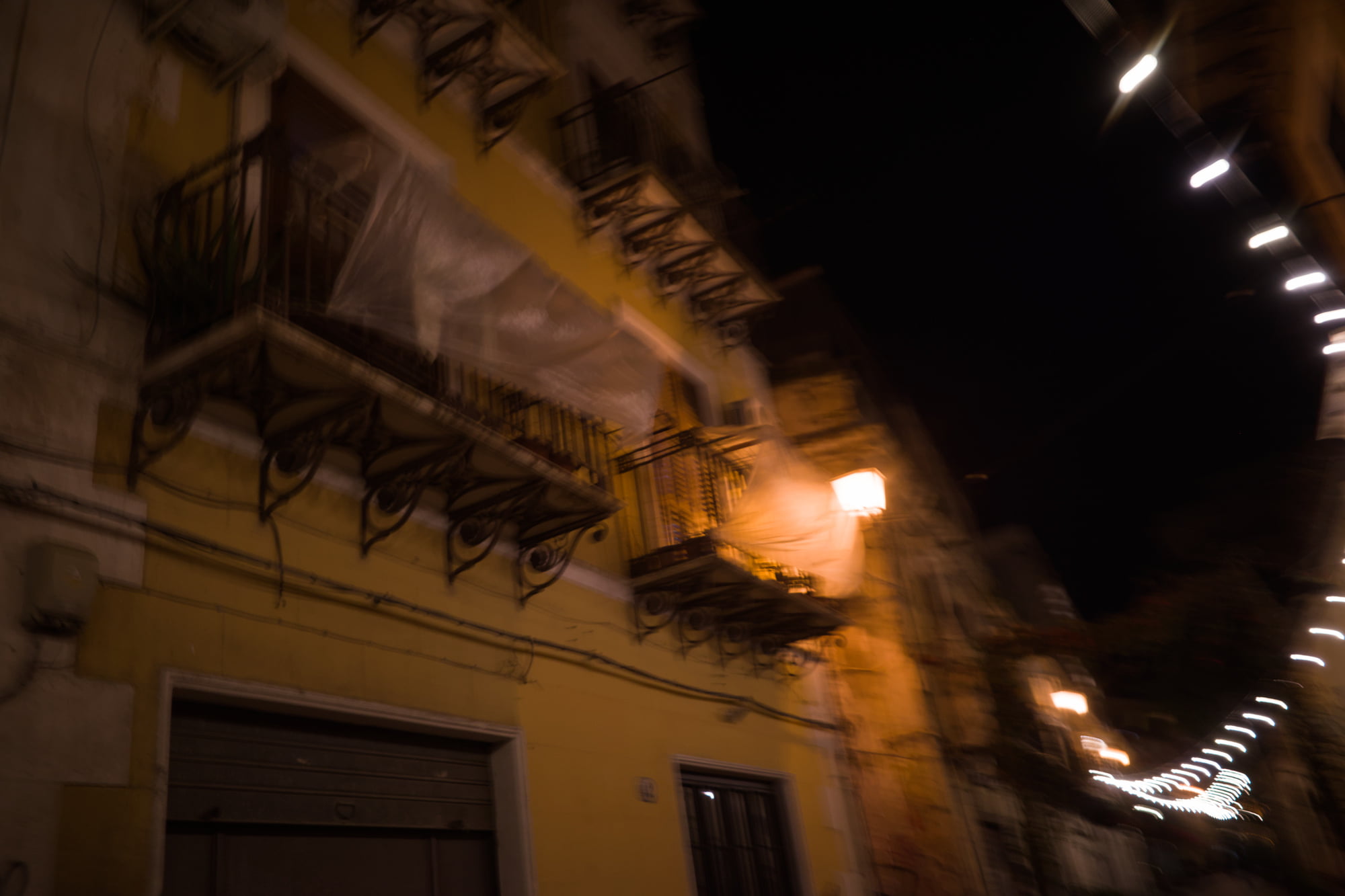 Motion-blurred night view of balconies, street lights, and a yellow building in Palermo