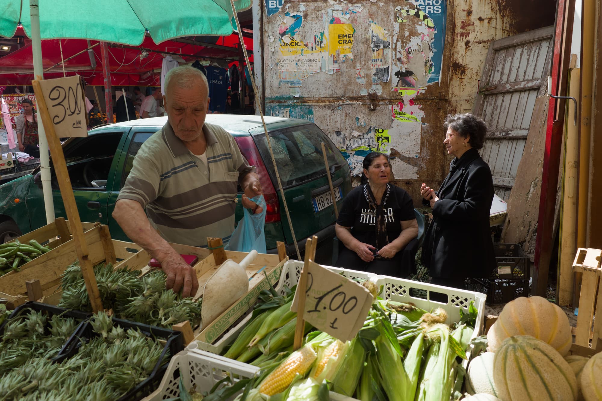 Vegetable market scene in Palermo with a vendor, two women talking, and crates of produce