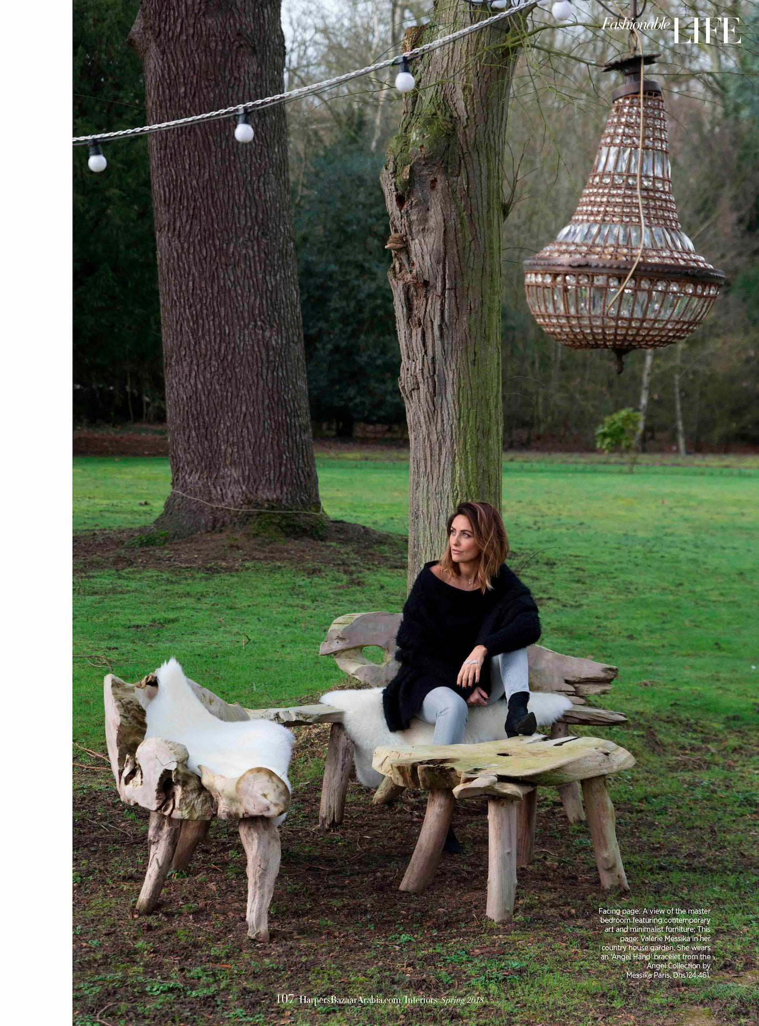 Valérie Messika seated outside on rustic wooden furniture in the garden of her country house